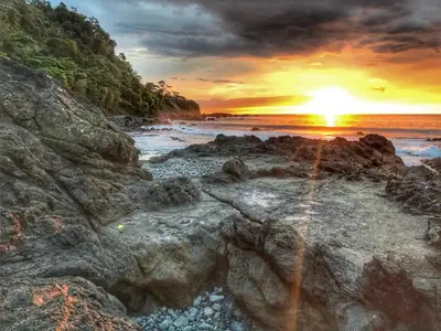 a sunset on the rocks at the beach at Macaws Ocean Club Apartamento # 18 in Jacó