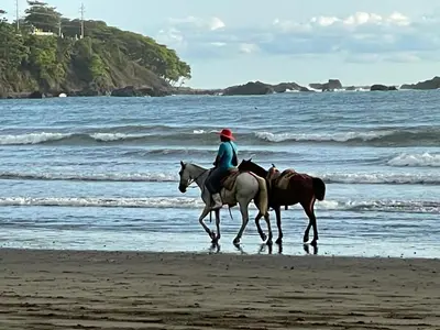 a person riding a horse on the beach at Macaws Ocean Club Apartamento # 18 in Jacó