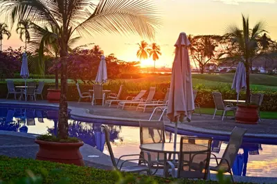 a pool with chairs and umbrellas in front of the sunset at HRG Condos at Los Sueños in Jacó