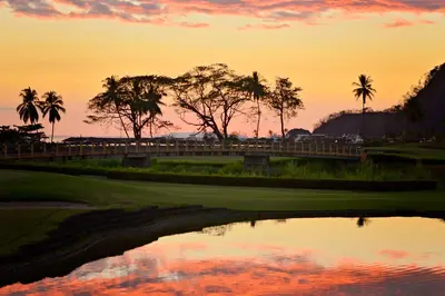 a golf course with palm trees and a pond at sunset at HRG Condos at Los Sueños in Jacó