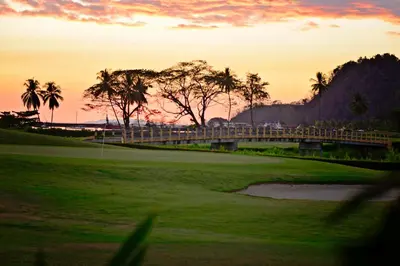a sunset over a golf course with palm trees and a bridge at HRG Condos at Los Sueños in Jacó