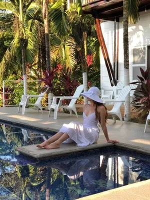 a woman in a white dress sitting next to a swimming pool at Ballena Dorada Lodge in Uvita