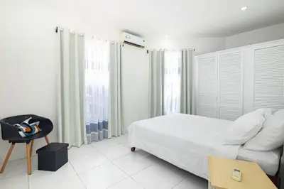 a white bedroom with a bed and a chair at Apartamentos Cristal in Quepos