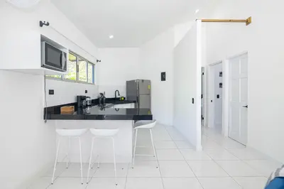 a white kitchen with a counter and stools at Apartamentos Cristal in Quepos