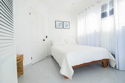 a white bedroom with a bed and a window at Apartamentos Cristal in Quepos