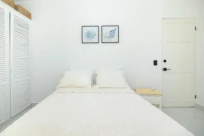 a white bedroom with a bed with two pictures on the wall at Apartamentos Cristal in Quepos