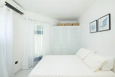 a white bedroom with a bed and a window at Apartamentos Cristal in Quepos