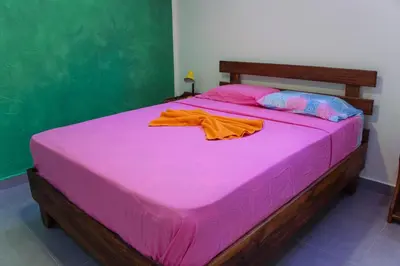 a pink bed with a pink blanket and an orange shirt on it at Casa Nelly Apartamentos in Sámara