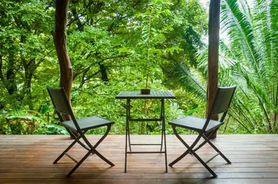 two chairs and a table on a deck with trees at Lodge Margouillat in Tambor