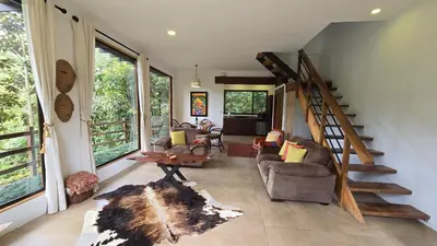 a living room with a staircase and chairs and windows at Monteverde Casa Mia, near main attractions and town! in Monteverde Costa Rica