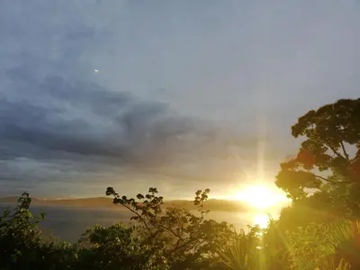 a sunset over a body of water with trees at Garden of Heliconias Lodge in Drake