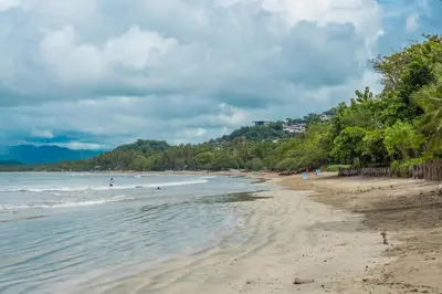 a beach with people in the water and trees at Casa Woodbine Private House on Tamarindo Beach in Tamarindo