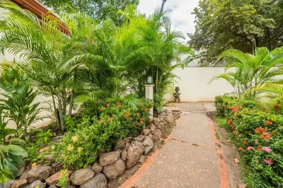 a walkway through a garden with flowers and palm trees at Casa Woodbine Private House on Tamarindo Beach in Tamarindo