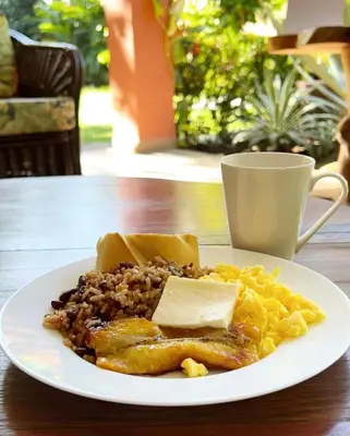 a plate of breakfast food on a table with a cup at Hotel Los Ranchos in Jacó