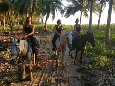 three women riding horses on a dirt road near palm trees at Calamocha Lodge in Santa Teresa Beach
