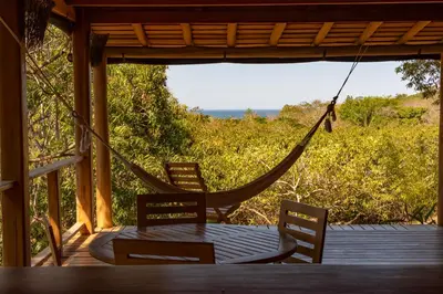 a hammock on a porch with a table and chairs at Calamocha Lodge in Santa Teresa Beach