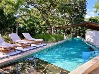 a swimming pool with two chairs and a gazebo at Villas Kalei in Playa Grande