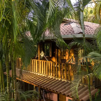 a house with a wooden balcony and palm trees at Salty Enthusiasts Share House & Villas in Santa Teresa Beach
