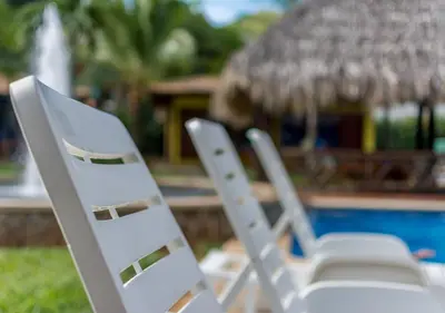 two white lawn chairs sitting next to a pool at Hotel Guanacaste Lodge in Playa Flamingo