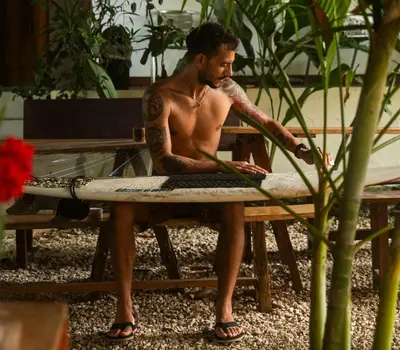 a man sitting on a bench holding a surfboard at La Posada - Hostel in Santa Teresa Beach