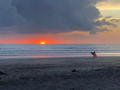 a person holding a surfboard on the beach at sunset at Boutique Hotel Luna Azul in Playa Ostional