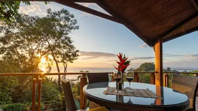 a table with wine glasses on a balcony with the sunset at Tulemar in Manuel Antonio