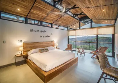 a bedroom with a bed and some chairs and windows at Pacific Kalokairi - Adults Only in Tamarindo