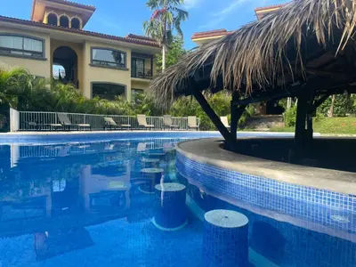 a resort swimming pool with a straw umbrella at The Oaks Tamarindo Pool Front Condominiums fast wifi in Tamarindo