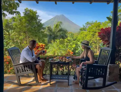 a man and woman sitting at a table with a mountain in the background at Arenal Manoa Resort & Hot Springs in Fortuna