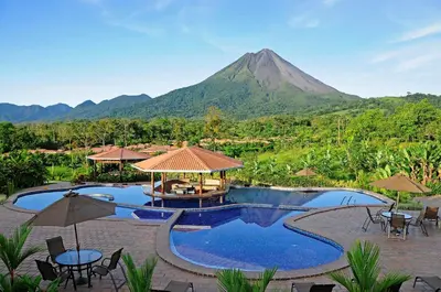 a resort with a pool with a mountain in the background at Arenal Manoa Resort & Hot Springs in Fortuna