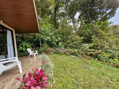 a porch with a white chair and a yard with flowers at Puma Meraki Mountain View Monteverde in Monteverde Costa Rica