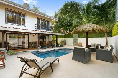 a house with a swimming pool with chairs and an umbrella at Spacious Home with Private Pool & Covered Patio Near the Beach in Playa Flamingo