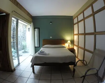a bedroom with a bed and a chair and a window at Hotel Guadalupe in Tilarán