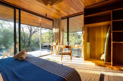 a bedroom with a blue bed in a room with large windows at Somos in Santa Teresa Beach