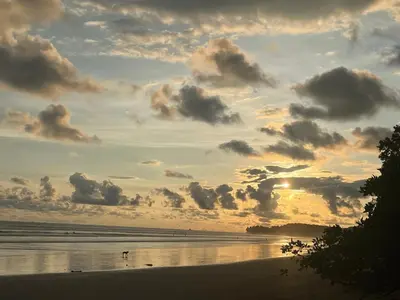 a sunset on a beach with people walking on the sand at Cabinas D’Val in Uvita
