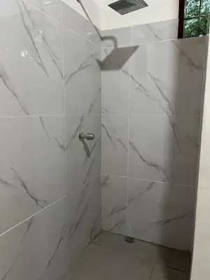 a bathroom with a shower with white marble walls at Woodstock Hostel in Sámara