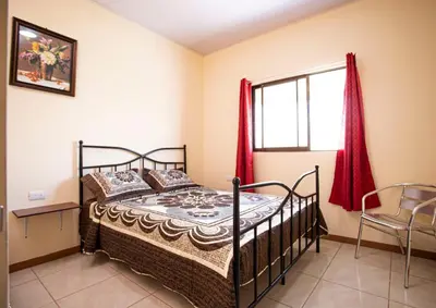 a bedroom with a bed and a window with red curtains at Flor de Katty Hostel Airport in Alajuela City