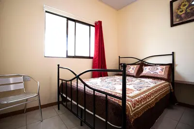 a bedroom with a bed and a chair and a window at Flor de Katty Hostel Airport in Alajuela City