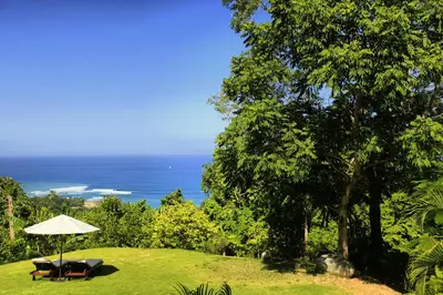 a bench and an umbrella on a field with the ocean at Villa Nimbu in Mal País
