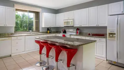 a kitchen with white cabinets and red bar stools at 3rd-floor space with modern décor recently renovated viewing over pool in Coco in Coco