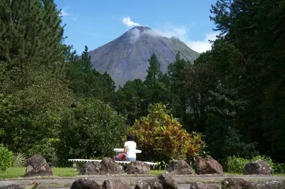 a woman sitting on a bench looking at a mountain at Arenal Observatory Lodge & Trails in Fortuna