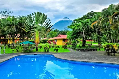 a resort with a pool and a mountain in the background at Hotel Arenal Country Inn in Fortuna