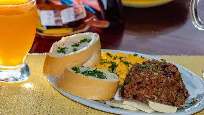a plate of food with meat and rice and a glass of beer at Hotel La Rosa de America in Alajuela City
