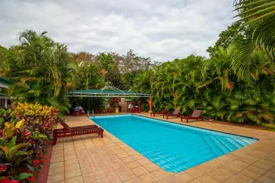 a swimming pool in a yard with benches and trees at Hotel La Rosa de America in Alajuela City