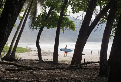 a person walking on the beach with a surfboard at Villa Flamingo in Santa Teresa Beach