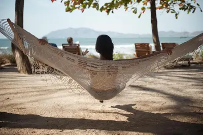 a woman sitting in a hammock on the beach at Capitán Suizo Beachfront Boutique Hotel in Tamarindo