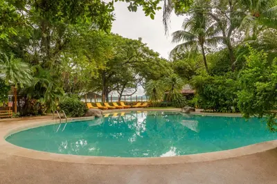 a swimming pool in a yard with trees at Capitán Suizo Beachfront Boutique Hotel in Tamarindo