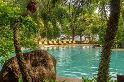 a swimming pool with palm trees and a large rock at Capitán Suizo Beachfront Boutique Hotel in Tamarindo