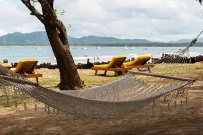 a hammock on a beach with chairs and the ocean at Capitán Suizo Beachfront Boutique Hotel in Tamarindo