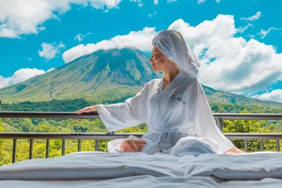 a woman sitting on a bed in front of a mountain at Hotel Arenal Kioro Suites & Spa in Fortuna